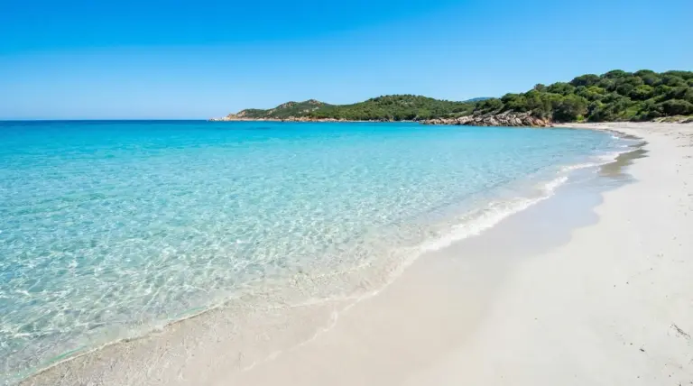 Spiaggia di sabbia bianca con mare turchese e costa verde, acqua cristallina in una baia tranquilla