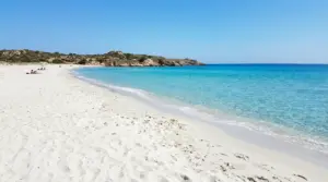 Spiaggia di sabbia bianca con mare turchese e costa rocciosa, con alcune persone in lontananza
