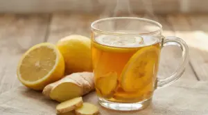 Tisana calda con zenzero e fette di limone in tazza di vetro su tavolo di legno