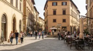 Centro storico pedonale con persone che passeggiano tra palazzi antichi, una fontana e tavolini all’aperto
